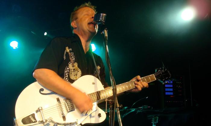 The lead singer for the Hillbilly Hellcats sings while strumming his guitar. 