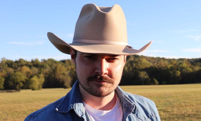 Jonathan Lee, wearing a light-colored cowboy hat and standing in front of a field