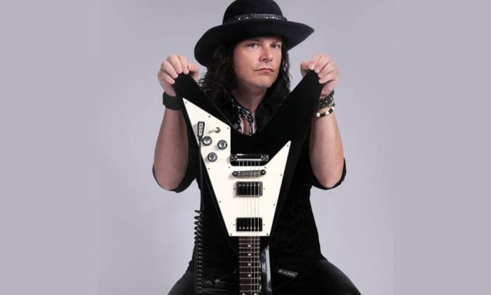 Anthony Gomes wears black clothing while posing with his guitar. 