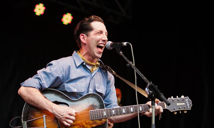 The musical artist Pokey LaFarge on stage at a microphone with his guitar