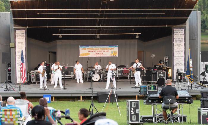 The U.S. Navy Cruisers band on an outdoor stage, wearing their white uniforms.