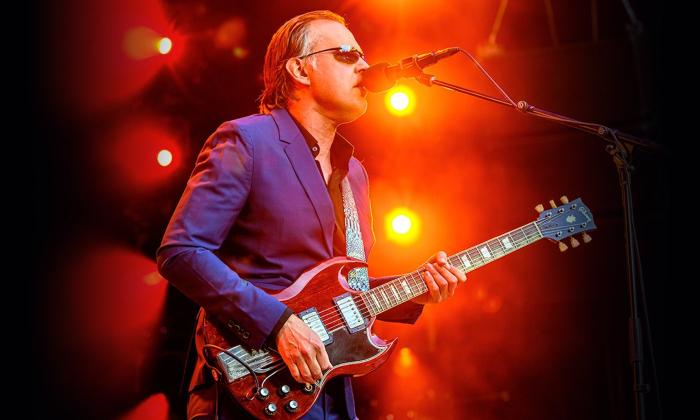 Joe Bonamassa wears a purple blazer and sings on stage for fans. 