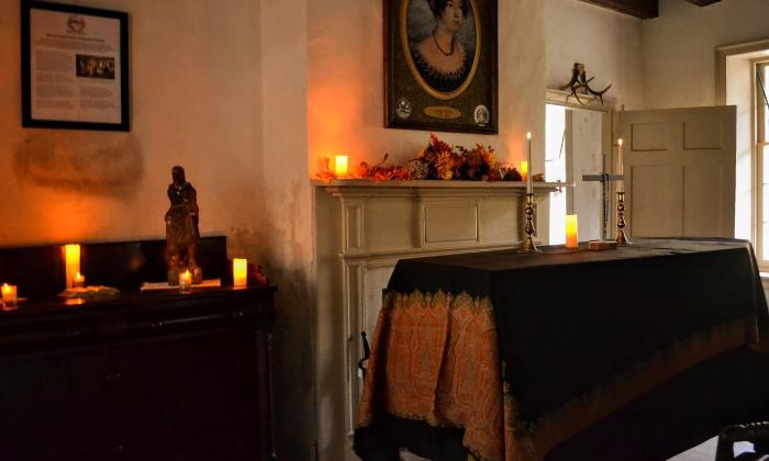 A casket, covered with a dark cloth and illuminated with candles