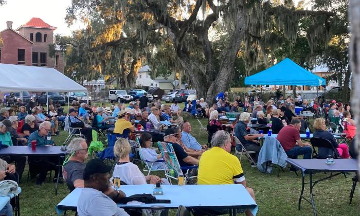 The audience at an outdoor blues and southern food fest sit at tables and in rows