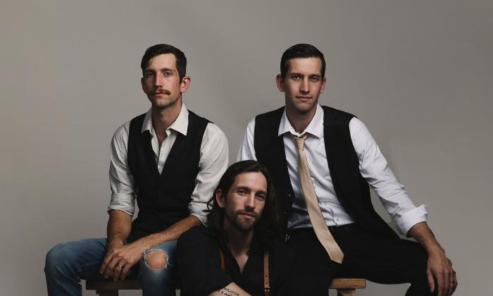 Three adult brothers, seated with one on the floor, all wearing black and white