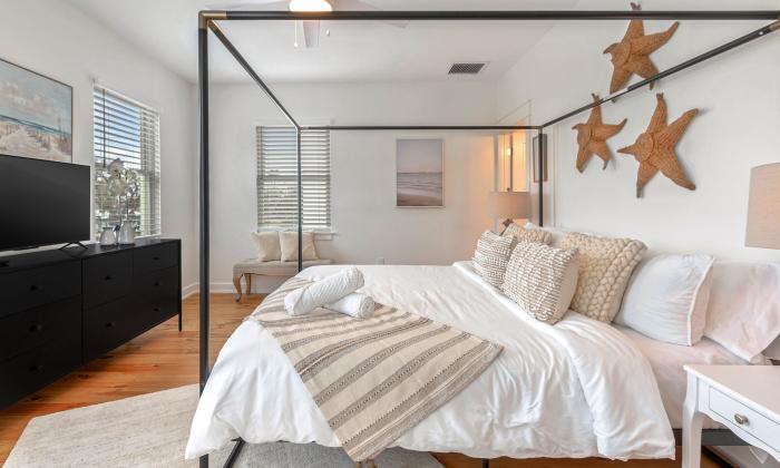 A master bedroom in a vacation home has a black frame over the bed and a star motif on the wall