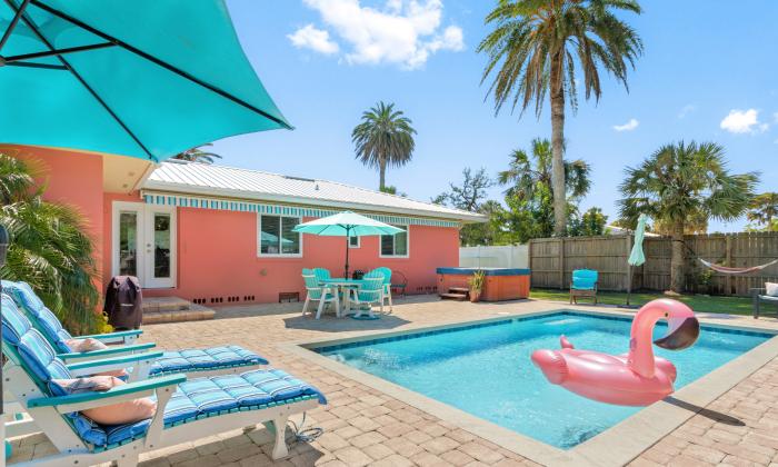 A coral-colored ranch home has a pool with lounge chairs and a table on the deck