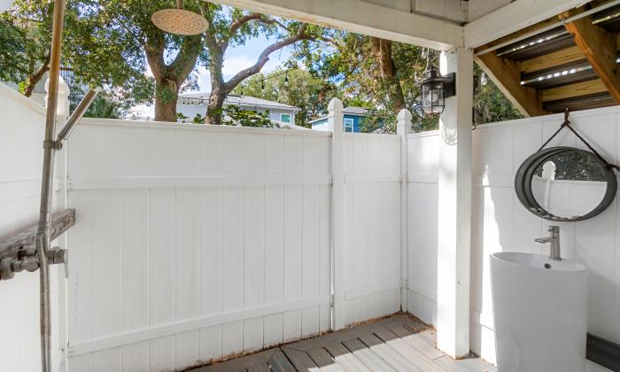 This fully-fenced outdoor shower has a sink and mirror