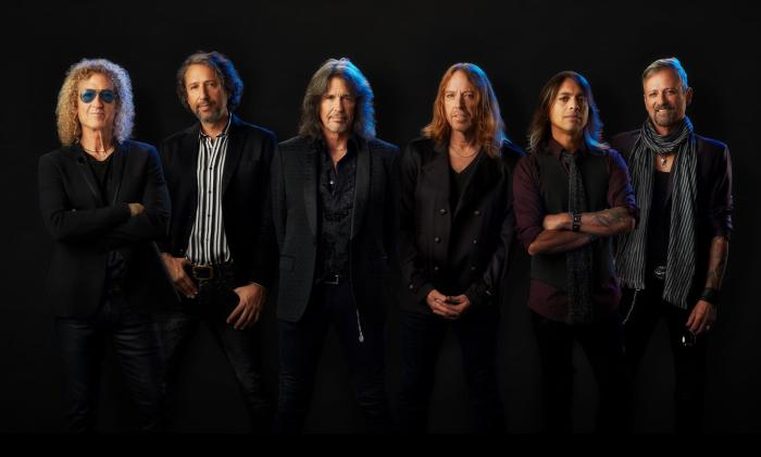 Bandmates from Foreigner pose in dark clothing in front of a black backdrop.