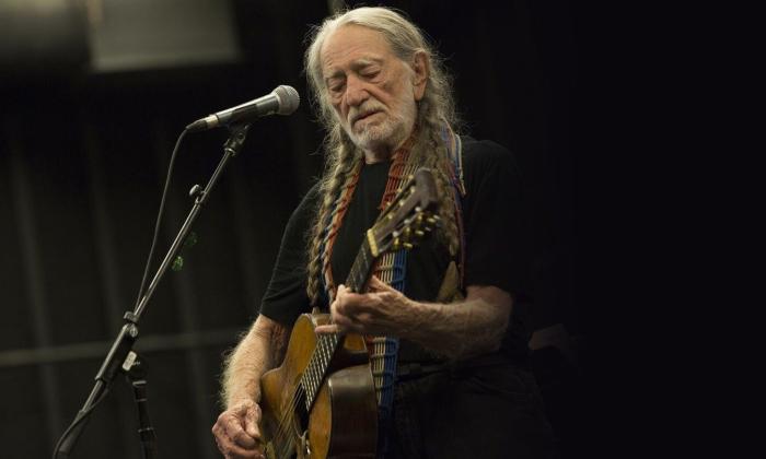 Willie Nelson performs on stage with his guitar.