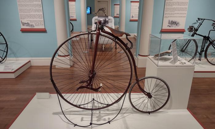 A vintage high-low bicycle on a white riser in a museum