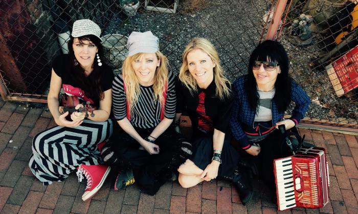 The four sisters of the Screaming Orphans, seated on a brick sidewalk