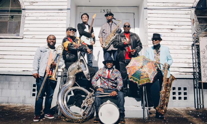 The seven members of the Dirty Dozen Brass Band, in front of an old, white building with their instruments