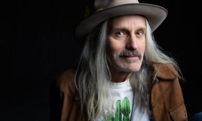 Steve Poltz poses in a white hat in front of a black backdrop.