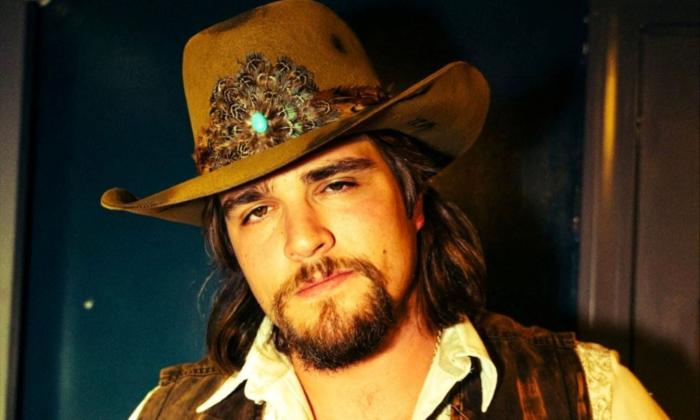 Gavin Adcock wears a brown cowboy hat and poses in front of a dark blue backdrop.