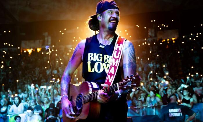 Michael Franti smiles while strumming his guitar. 