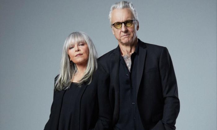 Pat Benatar & Neal Giraldo wear black and pose in front of a gray backdrop.