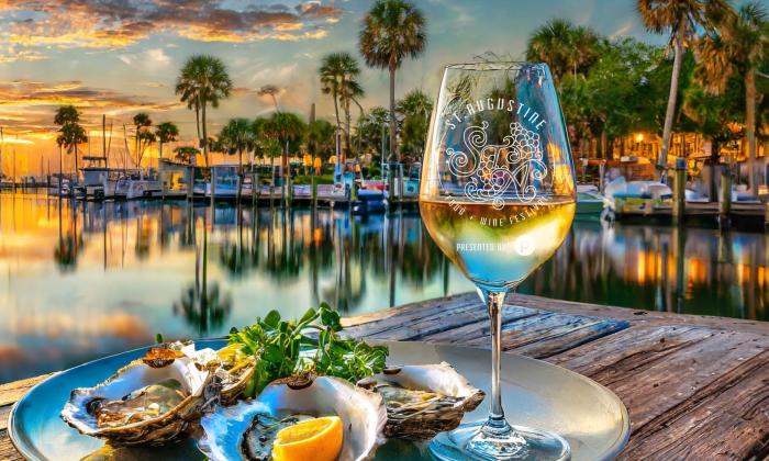 A glass of white wine and a plate of food sitting on a rustic table by the water