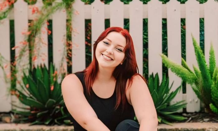 Musical performer Shayla Nelson, smiling, sitting in front of a picket fence. 