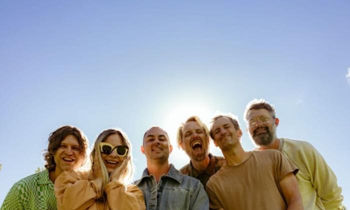 Bandmates from the Head And The Heart smile and pose in front of a blue backdrop.