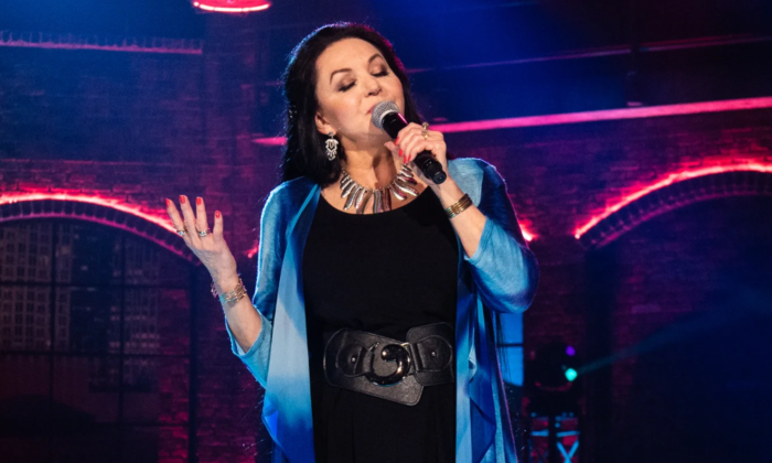 Crystal Gayle lifts her hand and sings on stage with her eyes closed.