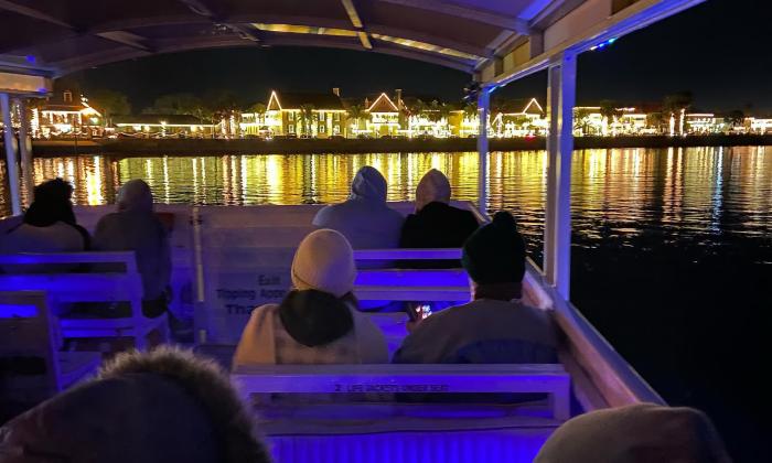 A tour boat, with passengers facing the brilliantly lit bayfront.