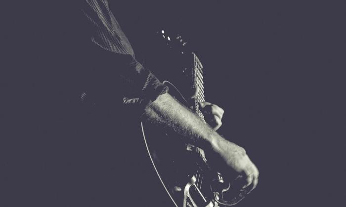 Jp Soars strums his guitar in front of a black backdrop.