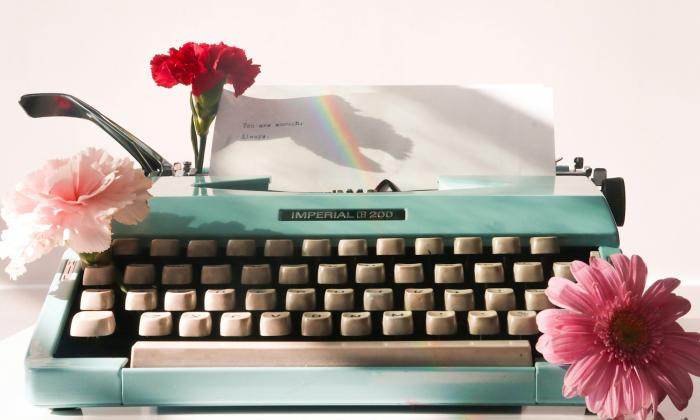 A green typewriter is positioned in front of a pink backdrop.