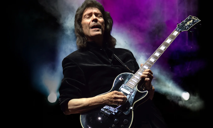Steve Hackett strums his guitar and performs on stage.