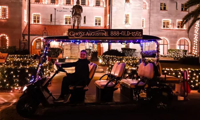 A driver in an electric vehicle waits for passengers in front of the holiday lights