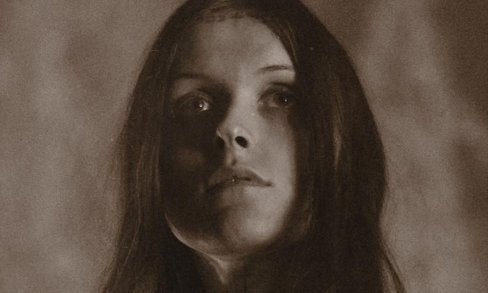 Ethel Cain poses before a richly textured background.