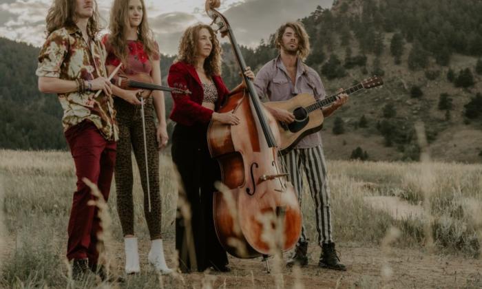 Bandmates from The Sweet Lilies stand with their instruments against a sweeping backdrop of trees and rolling hills.