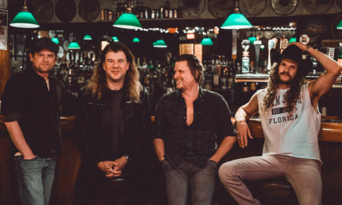Bandmates from Yarn sit on stools and pose in a bar.