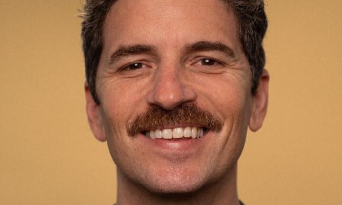 Zane Helberg smiles and poses in front of a mustard colored backdrop.