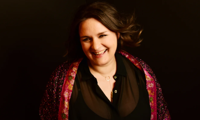Madeleine Peyroux wears a red scarf and poses in front of a black backdrop.