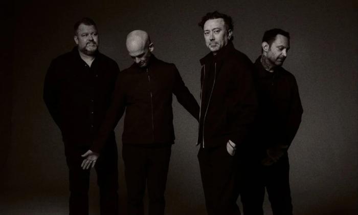 Bandmates from Rise Against wear dark clothing and pose in front of a black backdrop.