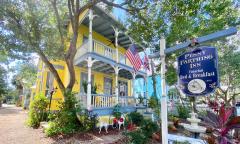 The exterior and sign of a brightly-painted yellow inn with blue and white trim