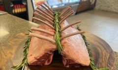 A rack of raw lamb with rosemary sprigs, artistically arranged and presented on a round wooden board