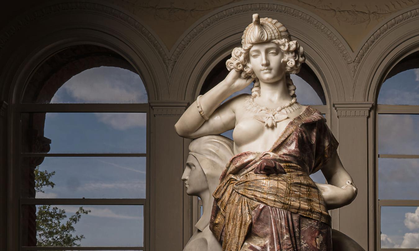 A sculpture from the Gilded Age, on display in front of a series of arch windows at the Lightner Museum