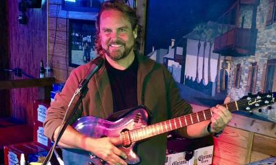 Wesley Ochs poses while clutching his guitar on stage. 