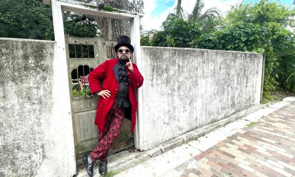 A man in red Steampunk garb leaning against a Spanish-style entryway