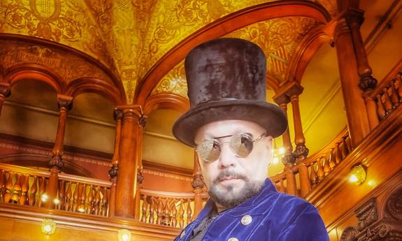 A photo of a man, close up, wearing a top hat and steampunk glasses, inside the Flagler entryway