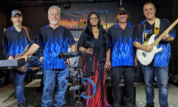 Five band members with black, blue, and red outfits standing on a stage