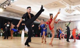 A ballroom of competing dancers, with two in the front showing their high kicks