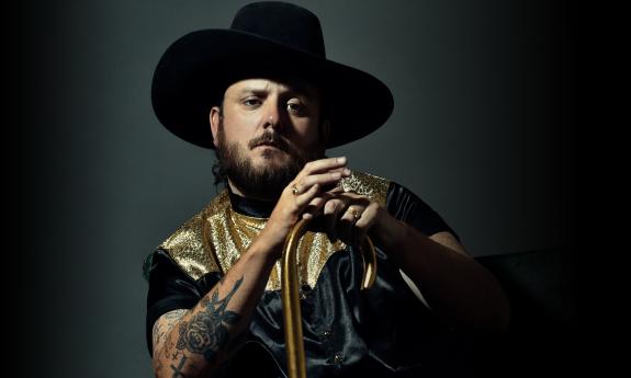 Paul Cauthen poses for the camera in front of a dark background. 