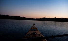 A beautiful sunset hovers over tranquil waters and a small yellow kayak.