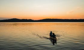 Two women smile as they kayak during sunset. 