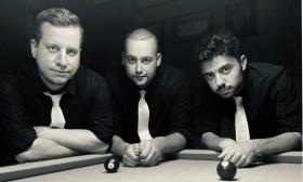 Ian, Matt, and Andre of Ferris Delux, leaning on a pool table while we wearing black shirts with skinny white ties