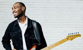 Guitarist Mathias Lattin with his guitar in front of white brick wall.