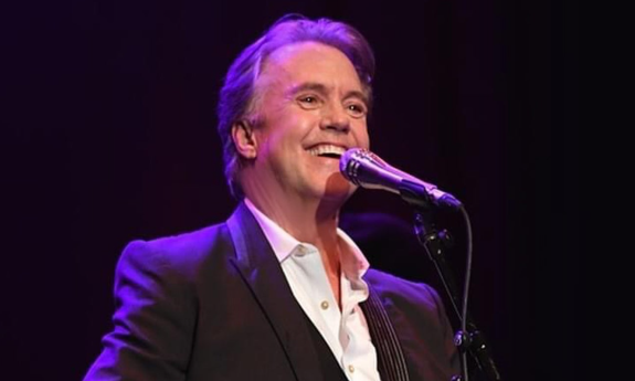 Shaun Cassidy smiles and sings with his lips positioned closely to the microphone. 